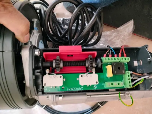 Motor de cierre metálico enrollable abierto, mostrando el sistema eléctrico y engranajes durante reparación profesional.